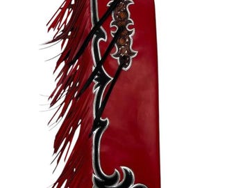 Op de afbeelding: Rode leren chaps met zwarte en zilveren decoratieve accenten. De chaps hebben franjes langs de zijkant en ingewikkelde bewerkingen aan de boven- en middenkant. Een kledingstuk in westernstijl.