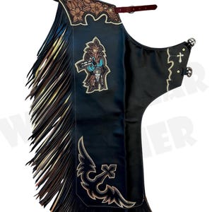 Puede incluir: Chaps de cuero negro con flecos marrones y beige. Los chaps presentan diseños florales y de cruz decorativos con un gráfico turquesa y marrón. La parte superior tiene una correa de cuero marrón y herrajes plateados.