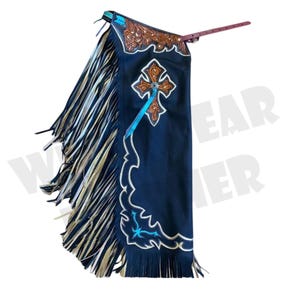 Puede incluir: Chaps de cuero azul marino oscuro con un diseño de cruz decorativa y costuras blancas. Los chaps presentan una parte superior de cuero marrón con repujado floral y largas flecos en los laterales. Una cinta turquesa acentúa la cruz.