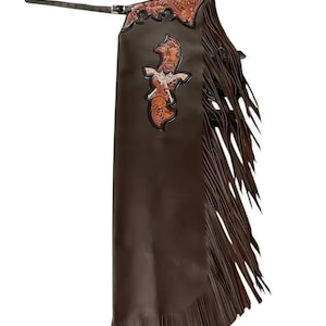Puede incluir: Chaps de cuero marrón con diseños florales y de pistolas decorativos. Los chaps tienen largas flecos a los lados y en la parte inferior, y un cinturón con hebilla. La parte superior tiene un patrón en relieve detallado.