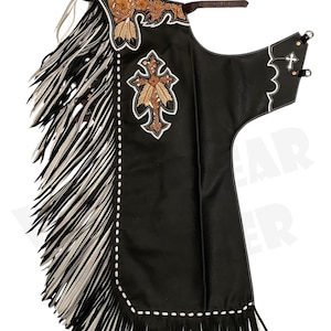Puede incluir: Chaps de cuero negro con flecos blancos y negros en los laterales e inferior. Los chaps presentan bordados decorativos florales y en forma de cruz en tonos marrones y beige. Un cinturón de cuero marrón y costuras blancas completan el diseño.