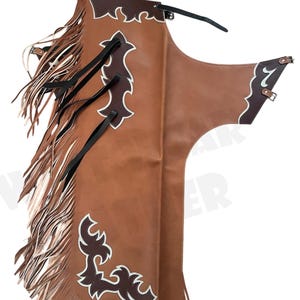 Puede incluir: Chaps de cuero marrón con detalles decorativos blancos y marrón oscuro. Los chaps tienen un borde con flecos y correas negras. El diseño incluye hebillas, adecuado para equitación o estilo western.