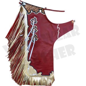 Puede incluir: Chaps de cuero rojo con flecos dorados y crema y diseños florales y de estrellas decorativos. Los chaps tienen un borde decorativo y cintas blancas. Los chaps están diseñados para montar a caballo.