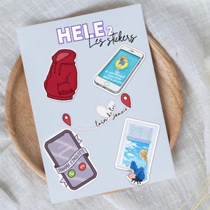 Peut inclure: Une planche d'autocollants avec divers motifs. Comprend un sweat à capuche rouge, un smartphone avec du texte, une scène de fenêtre et un cœur avec du texte. Les autocollants ont le texte "HELE 2 Les stickers" et d'autres textes en français.