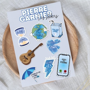 Può includere: Un foglio di adesivi con vari disegni, tra cui una clessidra, un mappamondo con un aeroplano di carta, un cartone di latte, una chitarra, un cuore, un ombrello blu e uno smartphone. Gli adesivi hanno testo in francese.