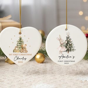May include: Two white ceramic Christmas ornaments. One is heart-shaped with a teddy bear and Christmas tree design, the other is round with a bunny and tree. Both say "My First Christmas" and a name, with the year 2025.
