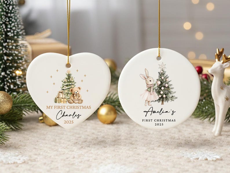 May include: Two white ceramic Christmas ornaments. One is heart-shaped with a teddy bear and Christmas tree design, the other is round with a bunny and tree. Both say "My First Christmas" and a name, with the year 2025.
