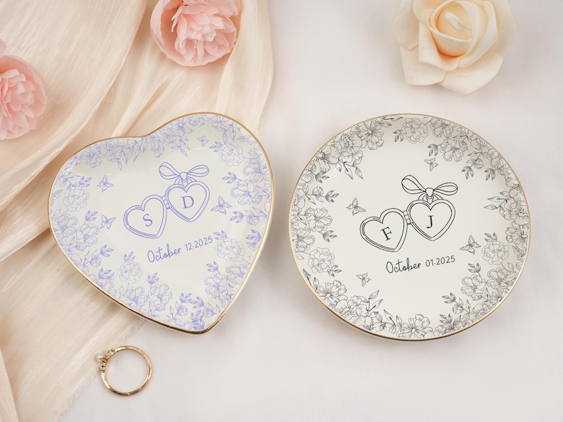 May include: Two personalized ring dishes, one heart-shaped and one round, with floral designs and gold rims. The heart-shaped dish has the initials "S" and "D" with the date "October 12, 2025". The round dish has the initials "F" and "J" with the date "October 01, 2025".