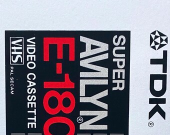 May include: A vintage TDK Super Avilyn E-180 VHS video cassette. The label features the text "HIGH OUTPUT HIGH RESOLUTION", "VIDEO CASSETTE", and "180 min. of video recording and playback". The cassette has a color bar indicator and the TDK logo.