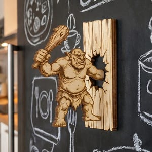 May include: A wooden wall decoration featuring a carved troll figure breaking through a wooden plank. The troll is holding a club. The background is a chalkboard with white chalk drawings of kitchen items.