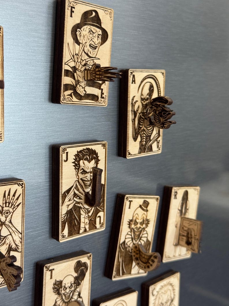 May include: Wooden playing card-shaped magnets featuring horror movie characters. Each magnet has a unique design, including Freddy Krueger, the Joker, and a skeletal figure. The magnets are brown with dark brown accents.