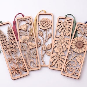 May include: Five rectangular wooden bookmarks featuring intricate laser-cut designs of lupines, poppies, a rose, monstera leaves, and a sunflower. Each bookmark is framed in light wood and includes a colorful silk tassel in green, maroon, yellow, or blue.