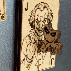 May include: Wooden magnet shaped like a playing card with a Joker illustration. The Joker is giving the middle finger and the text "WHY SO SERIOUS?" is visible. The magnet is made of light brown wood with dark brown edges.