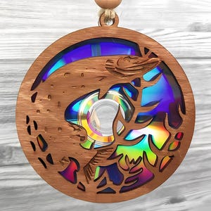 Könnte beinhalten: Runder Holzschmuck mit einem lasergeschnittenen Design, das einen Fisch und Wasserpflanzen zeigt. Der Schmuck hat eine regenbogenfarbene CD in der Mitte. Eine Holzperle und Bindfaden sind zum Aufhängen befestigt.
