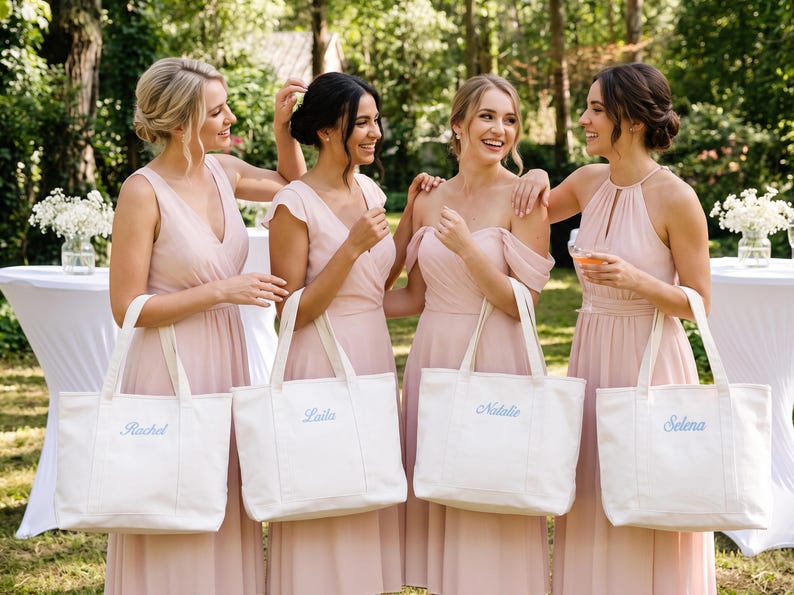 K&ouml;nnte beinhalten: Vier wei&szlig;e Tragetaschen aus Segeltuch, jede mit einem in hellblauer Schreibschrift gestickten Namen versehen. Die auf den Taschen angezeigten Namen sind Rachel, Laila, Natalie und Selena. Jede Tasche hat zwei stabile Griffe und einen rechteckigen Boden.