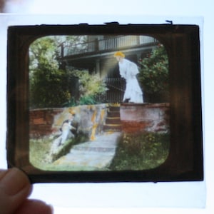 May include: A vintage black and white photograph of a woman in a white dress standing on a set of stone steps. A child is standing on the steps below her.