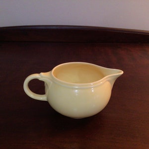 May include: A pale yellow ceramic creamer with a rounded body and a small handle.