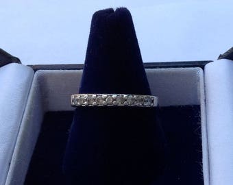 May include: A silver band ring with a row of small, clear gemstones set in a channel setting. The ring is displayed in a black velvet ring box.