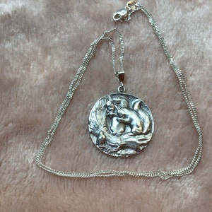 May include: A silver necklace with a round pendant featuring a detailed sculpture of two squirrels. The pendant is attached to a silver chain.