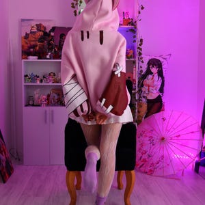 May include: A person wearing a pink hooded sweatshirt with bear ears, brown accents, and white bandages on the sleeves. The person is wearing white lace tights and purple boots. The word "ЦУНДЕРКА" is written in pink neon.