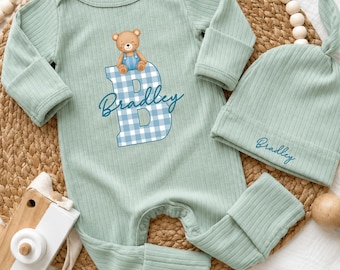 Può includere: Un set composto da una tutina a maniche lunghe in tessuto a coste verde salvia e un berretto annodato abbinato. La tutina presenta un orsetto marrone seduto su una grande lettera B a quadretti blu e bianchi con il nome Bradley in blu.