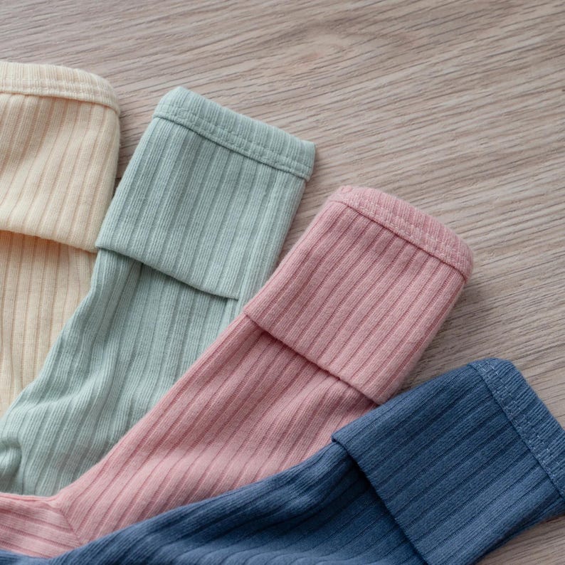 Pu&ograve; includere: Un set di quattro capi a maniche lunghe a coste nei colori crema, verde salvia, rosa antico e blu navy. Ogni capo presenta un polsino ripiegato all'estremit&agrave; della manica, che mostra una consistenza a coste verticali uniforme.