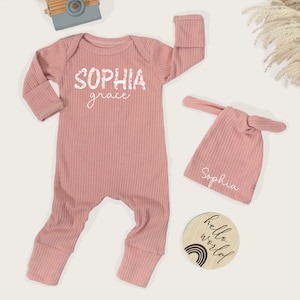 Pu&ograve; includere: Un completo per neonati rosa antico, composto da una tutina a coste con il nome "Sophia" e "grace" stampati sul davanti, un cappello annodato abbinato con "Sophia" e un disco di legno con "hello world" e un arcobaleno.