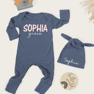 Pu&ograve; includere: Un completo per neonati in maglia a coste blu, composto da una tuta a maniche lunghe e un cappello annodato. La tuta presenta il nome "Sophia grace" in un design floreale e il cappello &egrave; ricamato con "Sophia". &Egrave; incluso anche un disco di legno con "hello world".