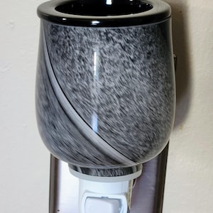 May include: A decorative night light with a black rim and a gray and white marbled design. The night light plugs into a wall outlet and has a white on/off switch.
