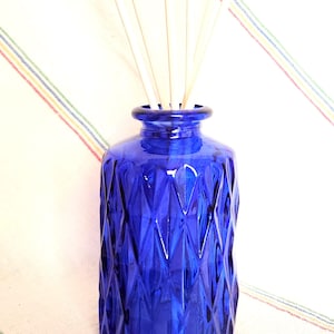 May include: A cobalt blue glass diffuser bottle with a diamond pattern. The bottle has wooden diffuser sticks inserted into the top.