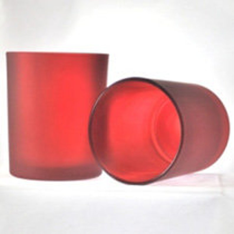 May include: Two frosted red glass candle jars. The jars are cylindrical and have a smooth, matte finish.