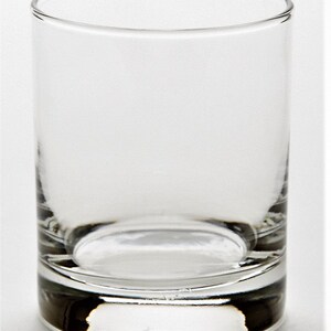 May include: A clear glass tumbler with a thick base. The glass is empty and has a smooth, rounded shape.