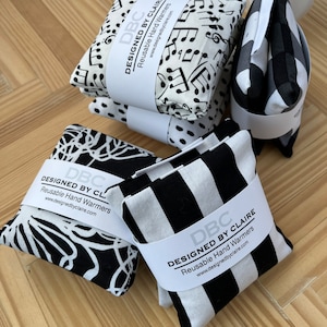 May include: Four black and white reusable hand warmers with the text "DBC Designed by Claire" and "Reusable Hand Warmers" on each. The warmers have different patterns: musical notes, floral, stripes, and a checkered pattern.