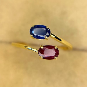 Può includere: Due anelli d'oro, ciascuno con una gemma ovale. Uno presenta uno zaffiro blu intenso, l'altro un rubino rosso intenso. Le gemme sono incastonate in una fascia d'oro, creando un design classico ed elegante.