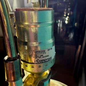 Pu&ograve; includere: Primo piano di un portalampada in ottone e argento con bordo marrone. Il portalampada ha un'etichetta con il testo "CRWRITERS LABORATORIES INC" e "Concept". La lampada &egrave; parzialmente assemblata.