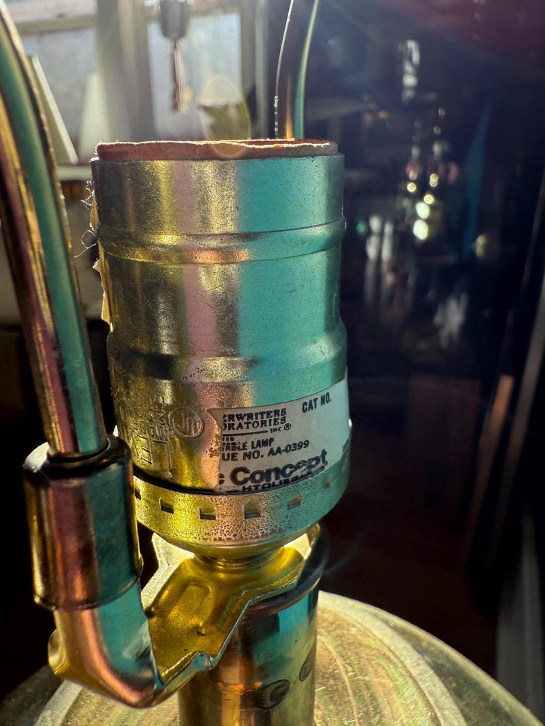Pu&ograve; includere: Primo piano di un portalampada in ottone e argento con bordo marrone. Il portalampada ha un'etichetta con il testo "CRWRITERS LABORATORIES INC" e "Concept". La lampada &egrave; parzialmente assemblata.