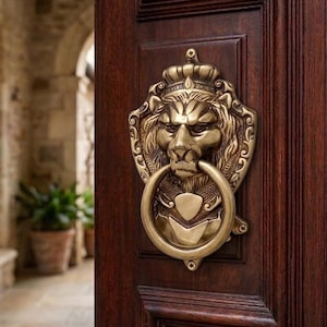 Pode incluir: Um aldravão de porta em latão com um design detalhado de cabeça de leão e um anel circular, montado numa porta de madeira castanho-escura com painéis embutidos e uma pequena placa de metal para a fechadura abaixo do aldravão na porta.