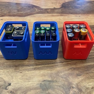 Könnte beinhalten: Drei farbige Batterie-Organizer. Ein blaues Behältnis mit der Aufschrift "9V" enthält 9-Volt-Batterien. Ein weiteres blaues Behältnis mit der Aufschrift "AAA" enthält AAA-Batterien. Ein rotes Behältnis mit der Aufschrift "AA" enthält AA-Batterien.