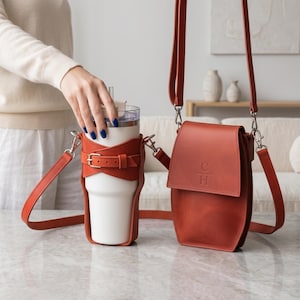 May include: A rust-colored leather cup holder with an adjustable buckle strap holding a white tumbler, paired with a matching rust-colored leather crossbody bag featuring a flap closure and the embossed letters C and H on the front.