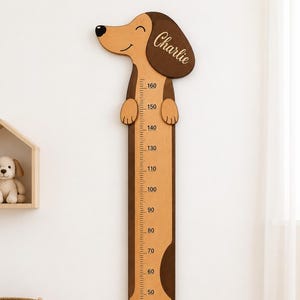 May include: A wooden dachshund-shaped height chart featuring a light and dark brown finish. The dog's head includes the name Charlie in script. A vertical metric scale from 30 to 160 centimeters is printed along the center of the dog's body.