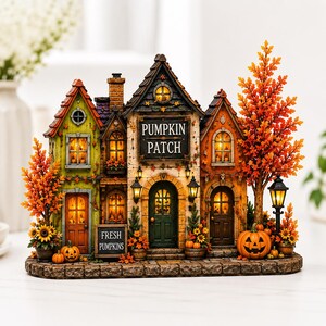 May include: A decorative miniature pumpkin patch building with illuminated windows, featuring a green house, a central structure with a PUMPKIN PATCH sign, and an orange house. It includes autumn trees, small pumpkins, and a FRESH PUMPKINS sign.