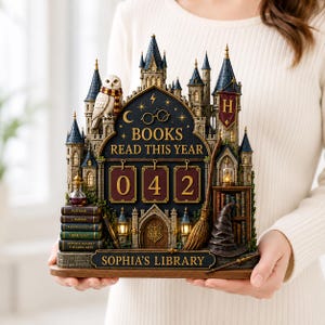 May include: A decorative tabletop display shaped like a castle, featuring the text 'BOOKS READ THIS YEAR' above three rotatable number tiles showing '042', and 'SOPHIA'S LIBRARY' at the base. It includes a white owl, a broom, and books.