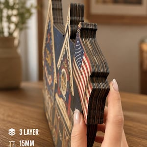May include: A three-layer plywood decorative sign with a 15mm thickness, featuring a printed American flag and architectural details. The object is constructed from stacked wood layers, showing a side profile with visible dark edges and textures.