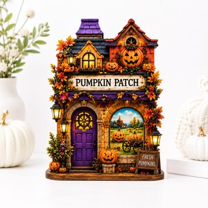 May include: A decorative miniature building labeled PUMPKIN PATCH with a purple door, orange pumpkin accents, and illuminated windows. The structure features autumn foliage, hanging lanterns, and a small sign reading FRESH PUMPKINS in front of a painted scene.