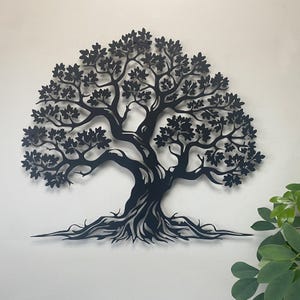 Könnte beinhalten: Schwarze Metall-Wandkunst eines Baumes. Der Baum zeigt ein detailliertes Design von Ästen, Blättern und Wurzeln. Das Kunstwerk ist an einer weißen Wand befestigt, was einen auffälligen Kontrast erzeugt. Die Silhouette des Baumes ist aufwendig gestaltet.