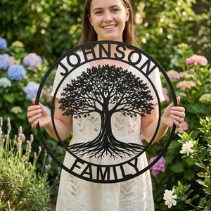 Peut inclure: Décoration murale en métal noir représentant un arbre généalogique avec le nom de famille "JOHNSON" en haut et "FAMILY" en bas. Le motif de l'arbre présente un tronc, des branches et des racines détaillés dans un cadre circulaire.
