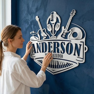 Peut inclure: Panneau métallique blanc avec des instruments de musique et le nom "ANDERSON STUDIO" sur un mur bleu. Le panneau représente un microphone, des écouteurs, des guitares, une batterie, un disque vinyle et un clavier de piano.