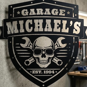 Peut inclure: Panneau de garage en métal noir avec le texte "GARAGE MICHAEL'S" et "EST. 1994". Le panneau représente un crâne portant des lunettes de soleil avec des clés croisées.