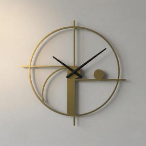 May include: A gold-coloured metal wall clock featuring a circular frame with a vertical bar and a horizontal line intersecting the centre. The clock has two black hands and a small gold circular accent positioned on the right side of the horizontal bar.