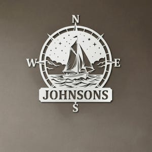 Personalized nautical compass metal wall decor featuring a sailboat at sea with custom family name, designed in a round coastal style. Available in multiple sizes and finishes including black, gold, silver, bronze, and white. Ideal for living rooms, entryways, beach houses, lake houses, or outdoor walls. Easy to hang and weather resistant. A unique gift for sailors, ocean lovers, housewarming, weddings, or modern coastal home decor.